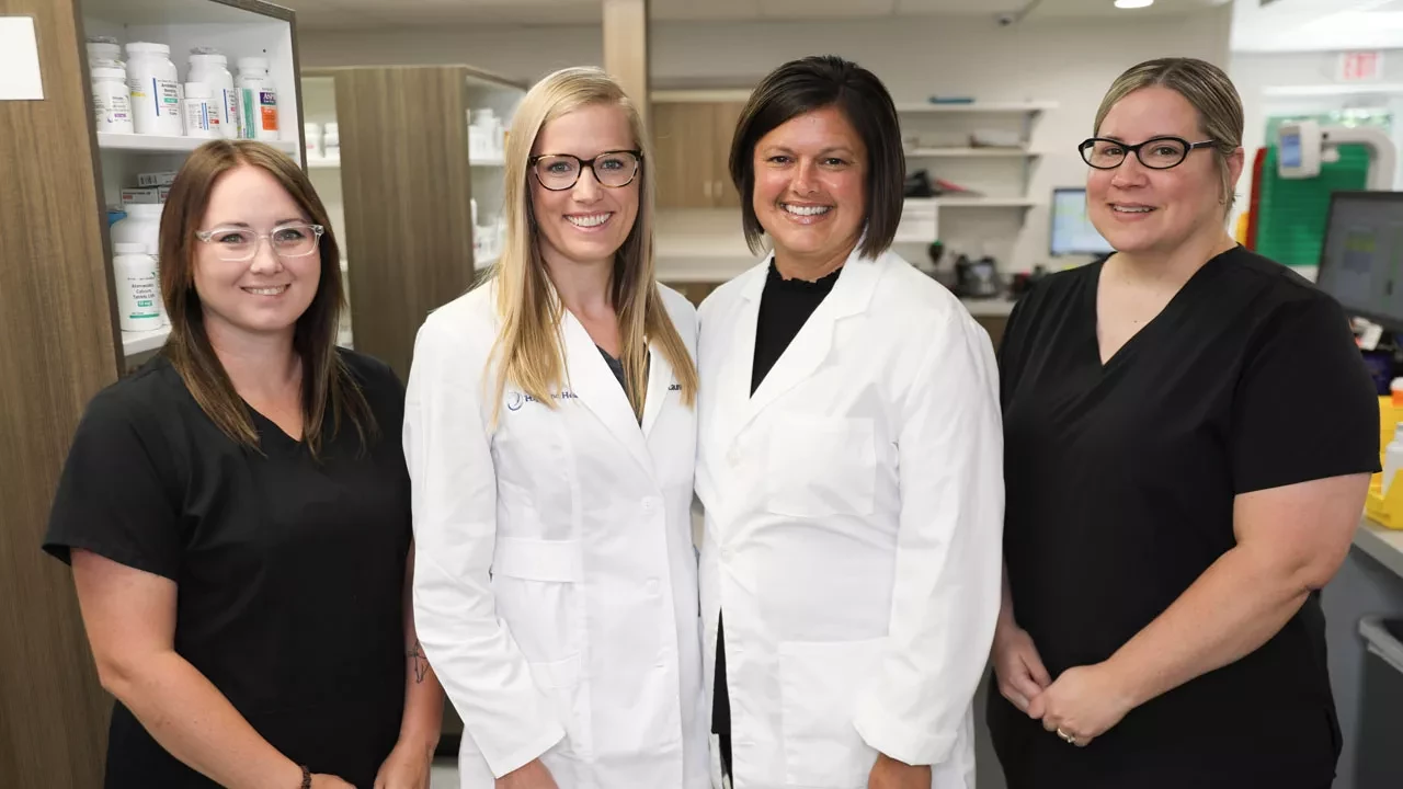 Group of healthcare professionals in white coats and scrubs standing in a pharmacy at Highland Health Providers.